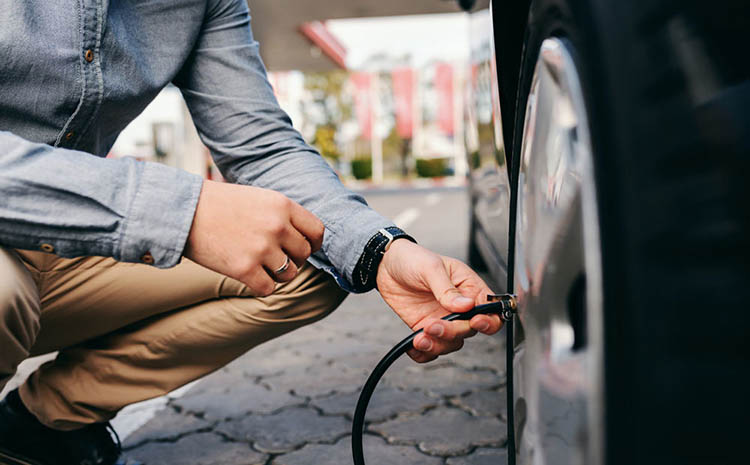 راننده در حال بررسی و تنظیم فشار باد تایر خودرو با استفاده از پمپ باد